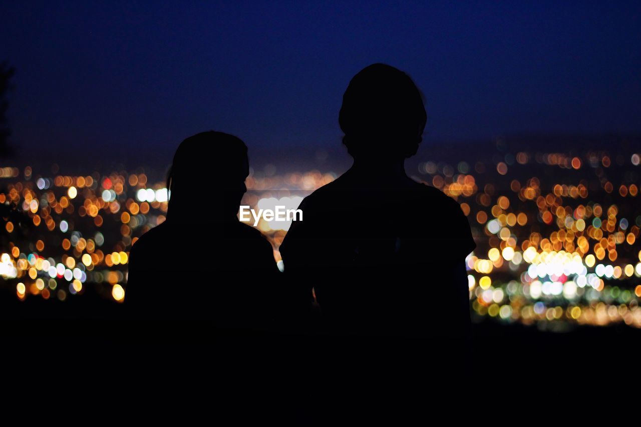 Rear view of silhouette couple against illuminated city at night