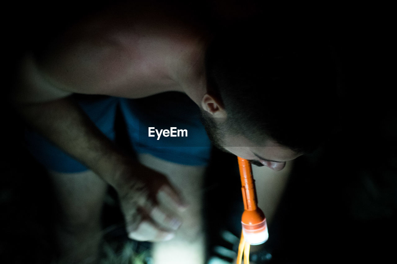 Man with flashlight bending on field at night