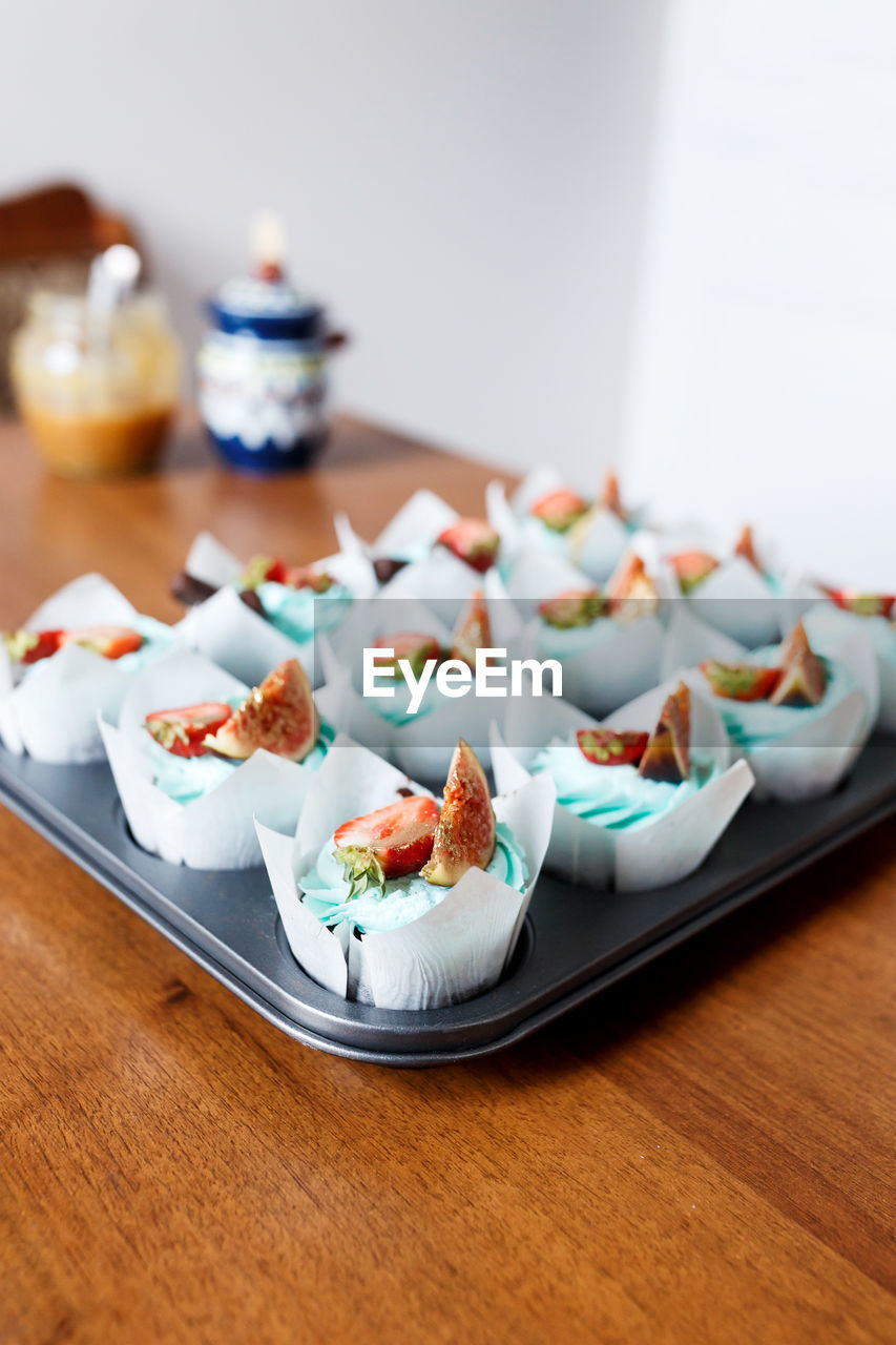 The plate of tasty cupcakes decorated with strawberry, fig and cream