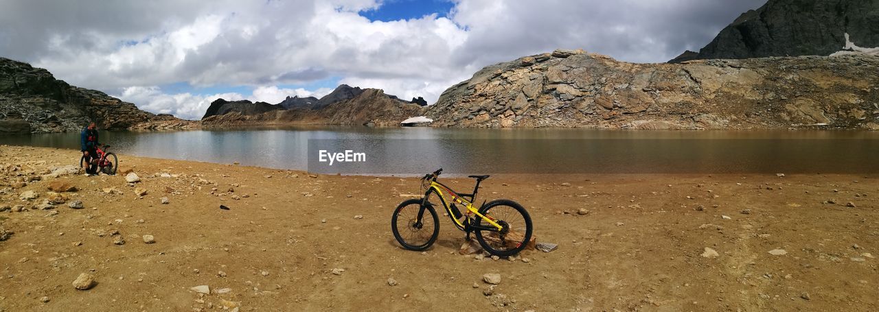 BICYCLES ON LAKE BY MOUNTAIN AGAINST SKY