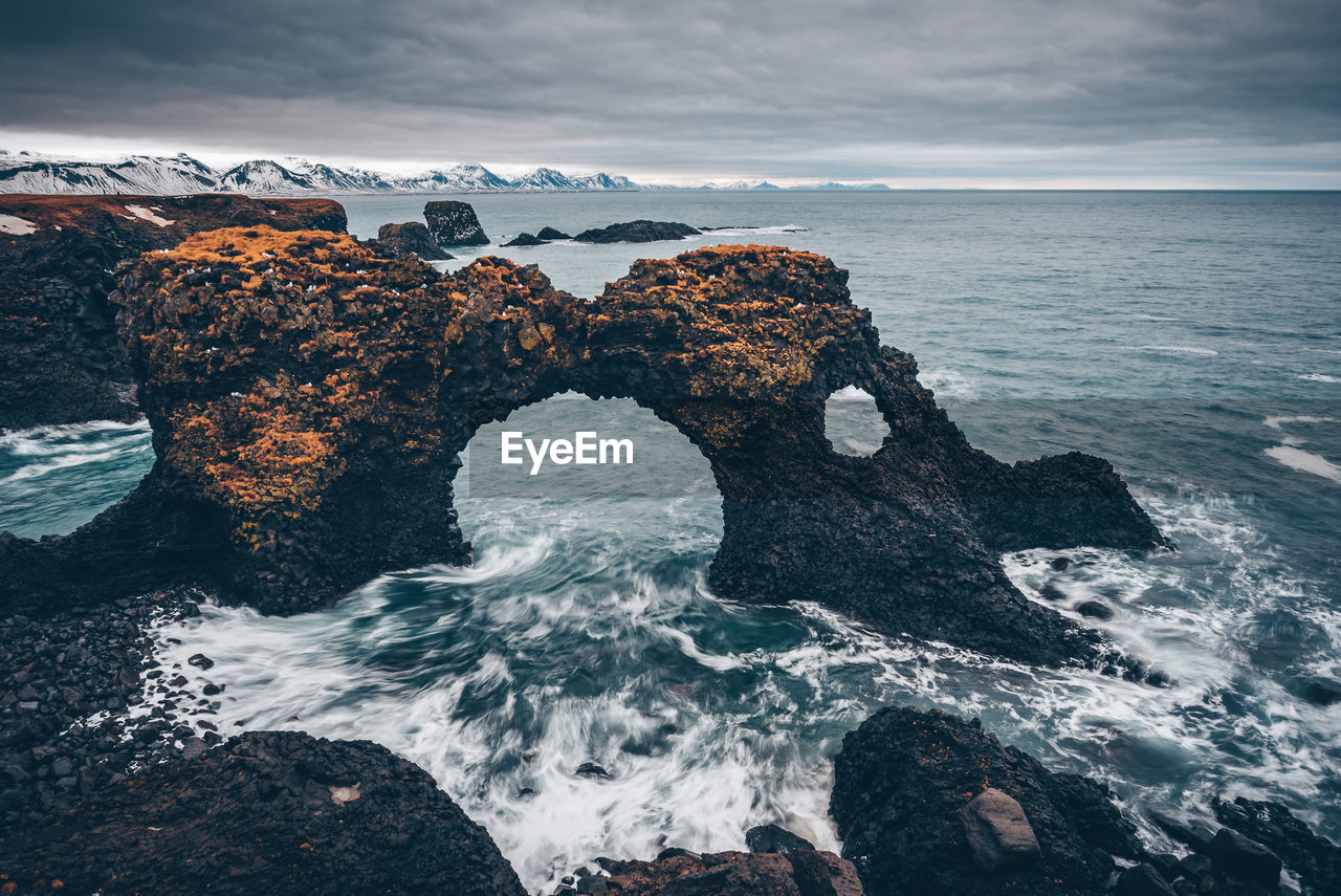 Rock formation in sea against cloudy sky