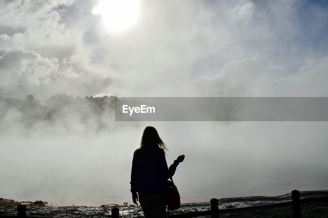 Silhouette of woman standing on landscape against cloudy sky