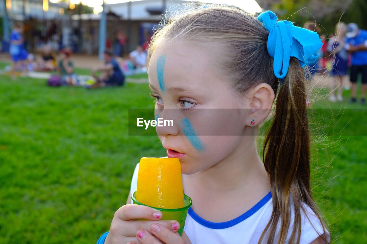 Girl with face paint having flavored ice on grassy field