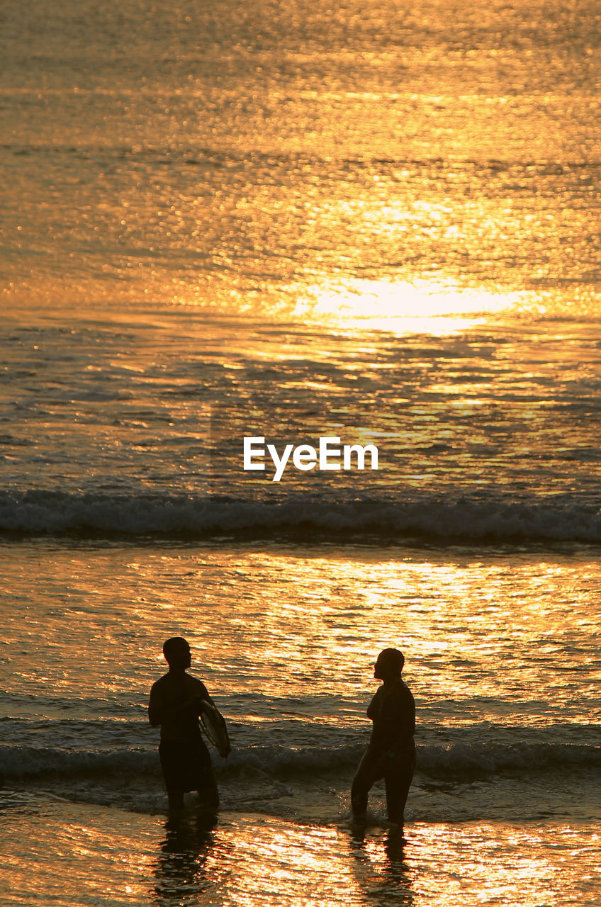 Silhouette friends standing at beach during sunset