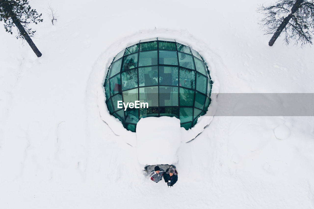 Aerial view of male friends standing at hotel amidst snow covered field