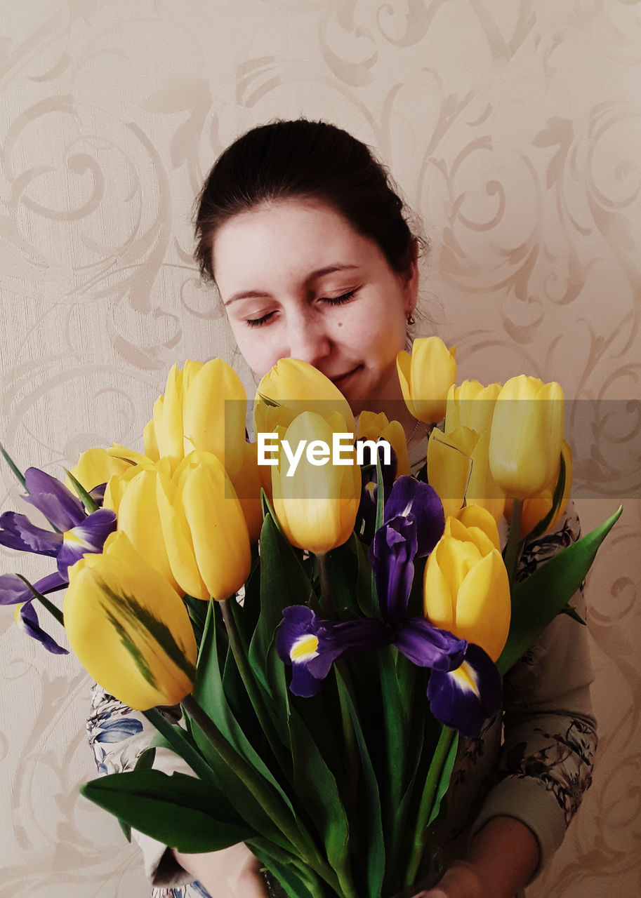 Young woman smelling bunch of tulips and iris against wallpaper