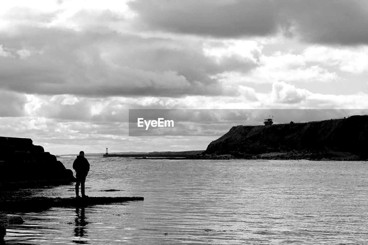 Rear view of man standing on rock in bay against sky