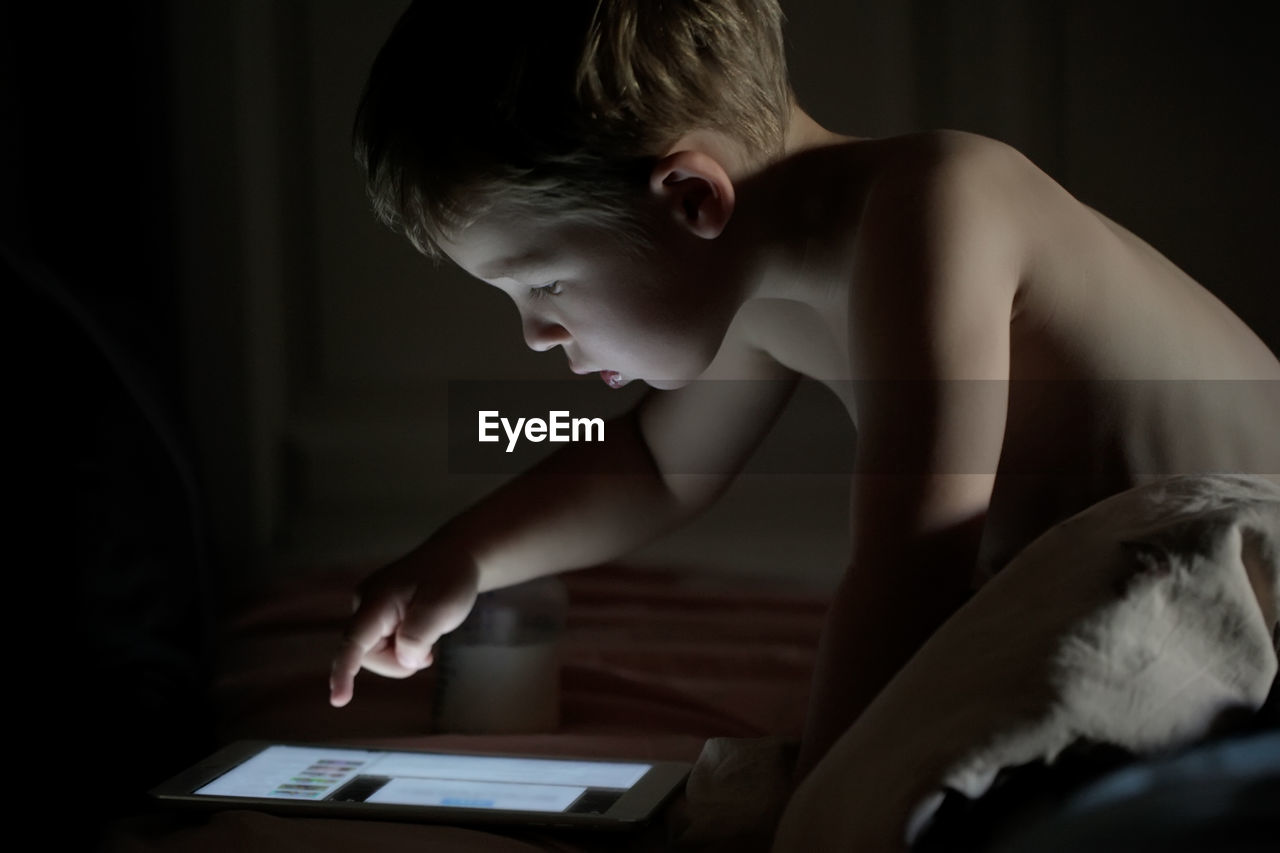 Close-up of shirtless boy using digital tablet at home