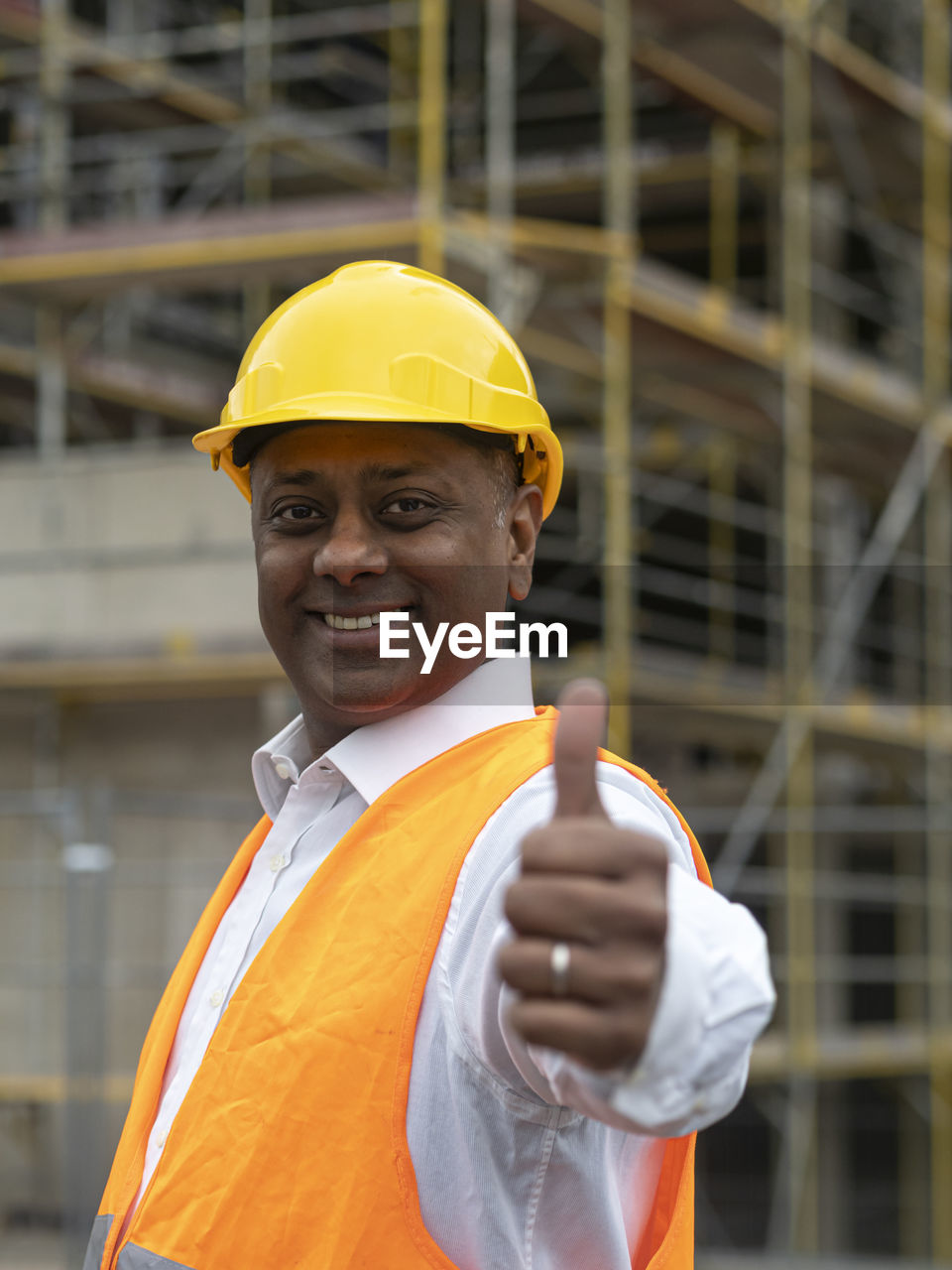 Smiling indian construction worker posing looking at the camera and showing a thumbs up gesture