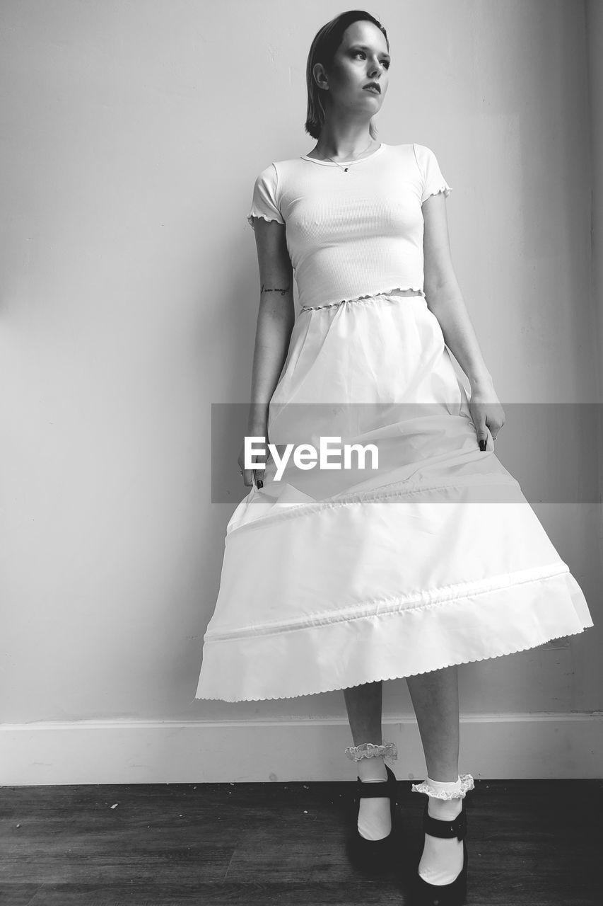 Young woman looking away while standing against wall