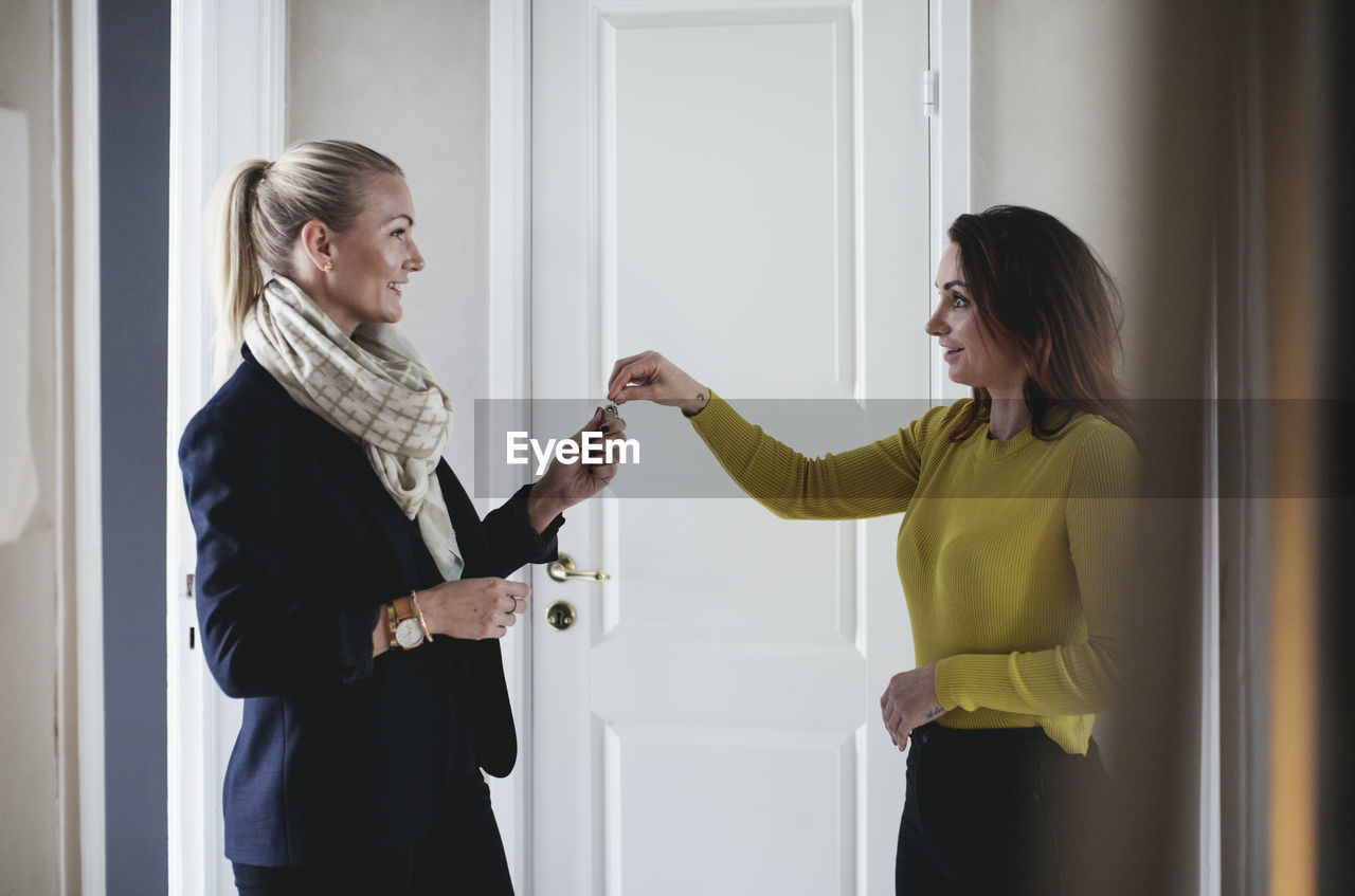 Smiling businesswoman giving key to colleague at home