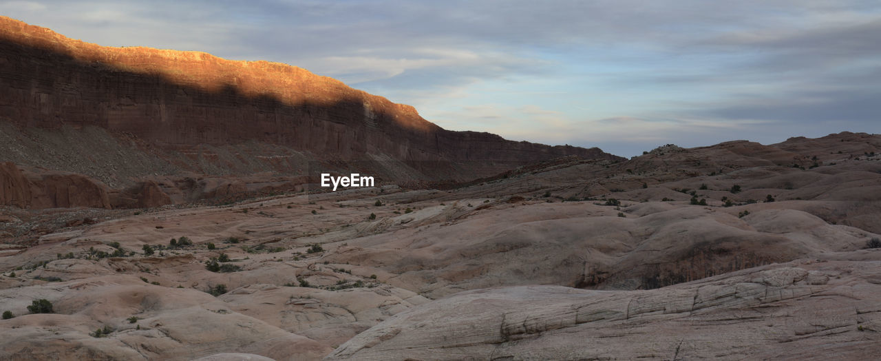 Flash of light on halls mesa cliffs at sunset above rolling slickrock.