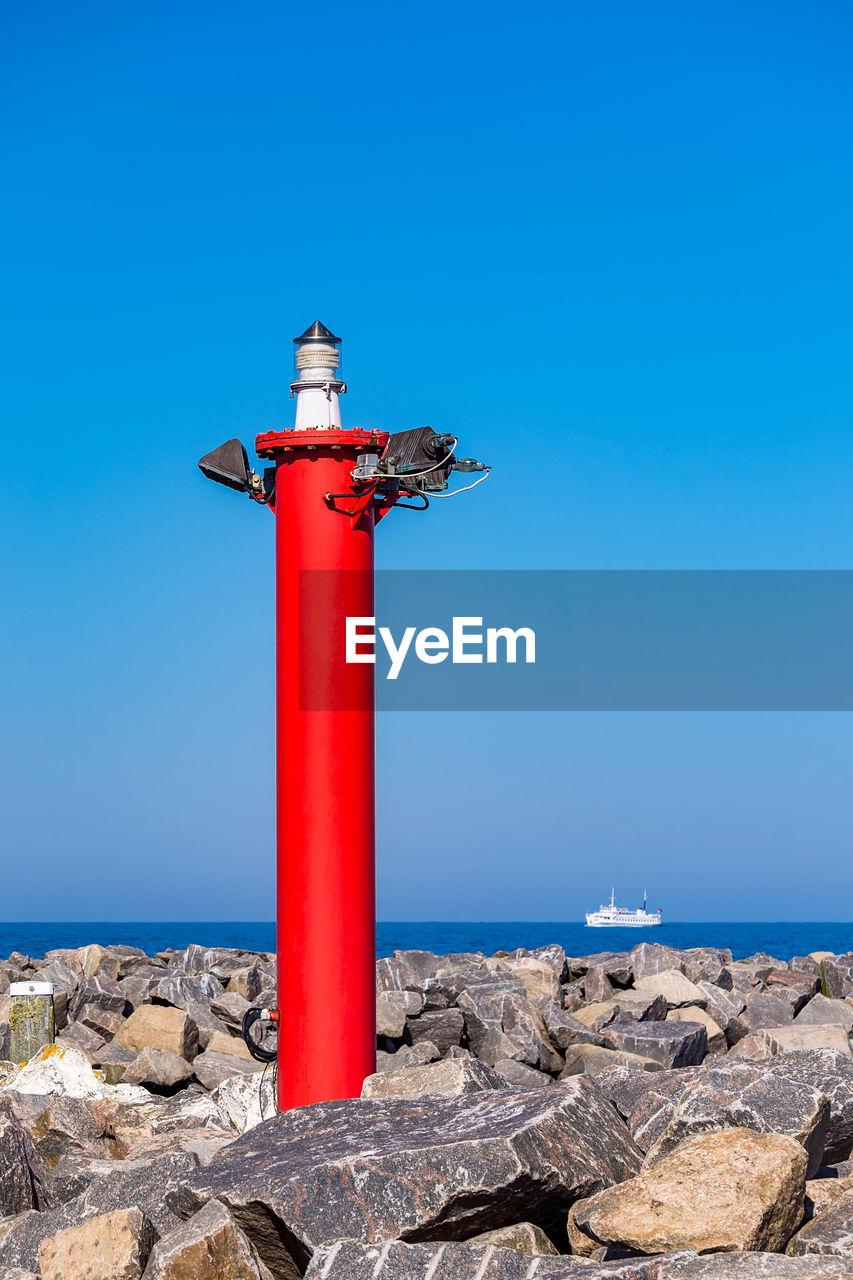 Lighthouse by sea against clear blue sky