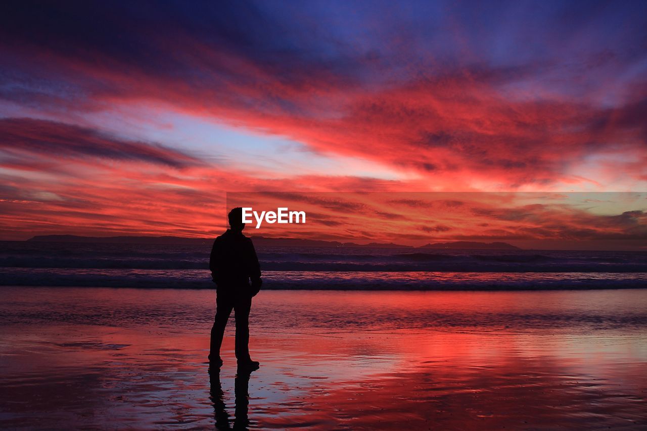 Full length rear view of man standing at beach during sunset