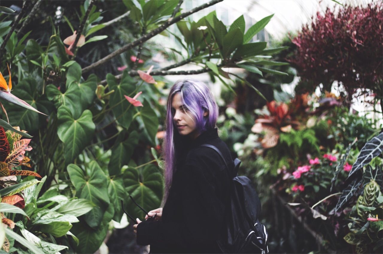 Portrait of young woman standing amidst plants in garden