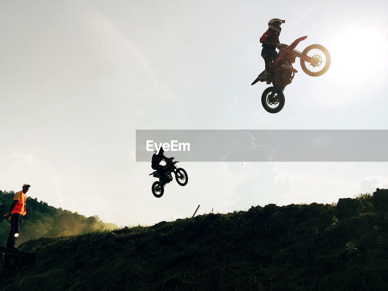 Low angle view of silhouette bikers with motorcycles jumping against sky