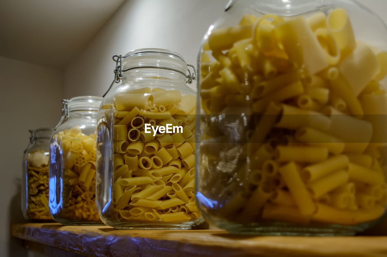 Four glass jars standing on the shelf and filled with various types of pasta.