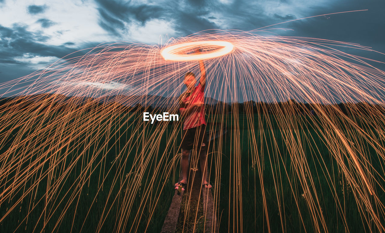 Low angle view of man spinning wire wool against sky during dusk