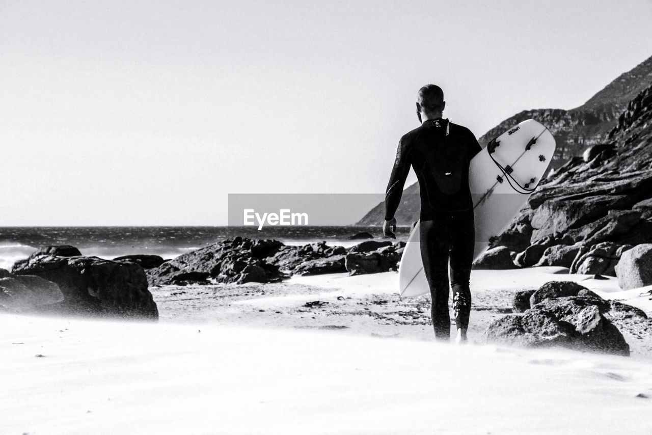 Rear view of man carrying a surfboard on beach