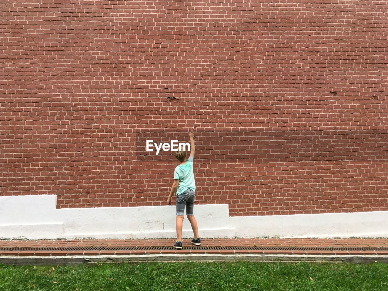 Rear view of boy standing against brick wall