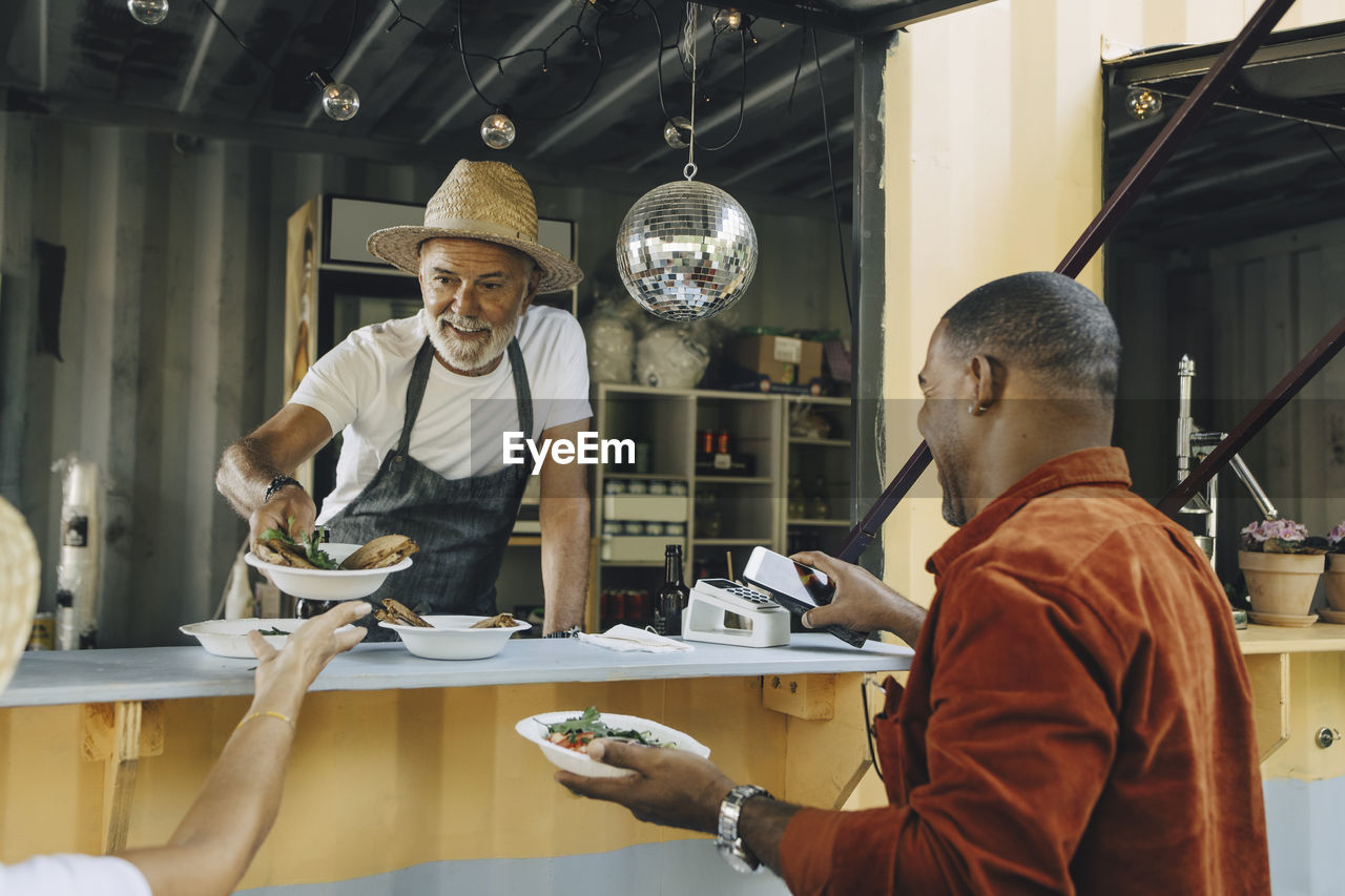 Seller serving food while male customer doing contactless payment through smart phone