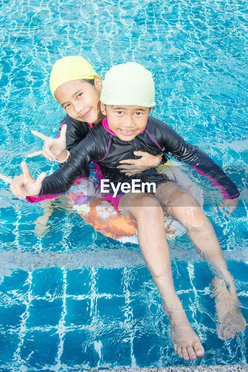 Portrait of siblings gesturing while swimming in pool