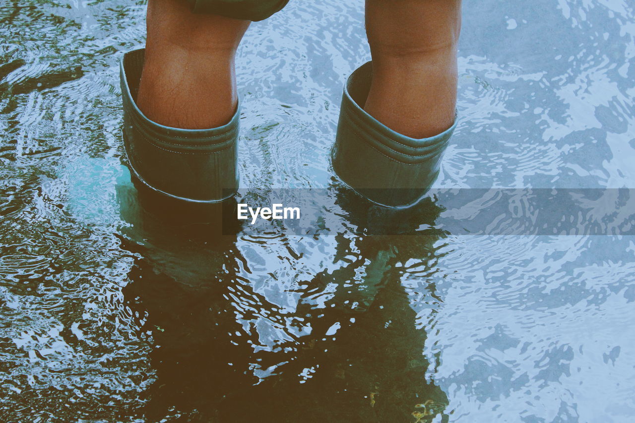 Low section of person wearing rubber boots while standing in water