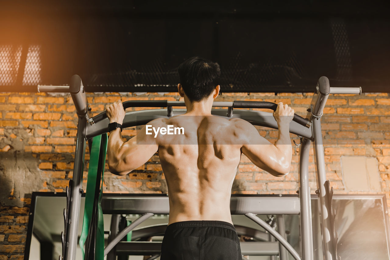 Rear view of shirtless man exercising at gym