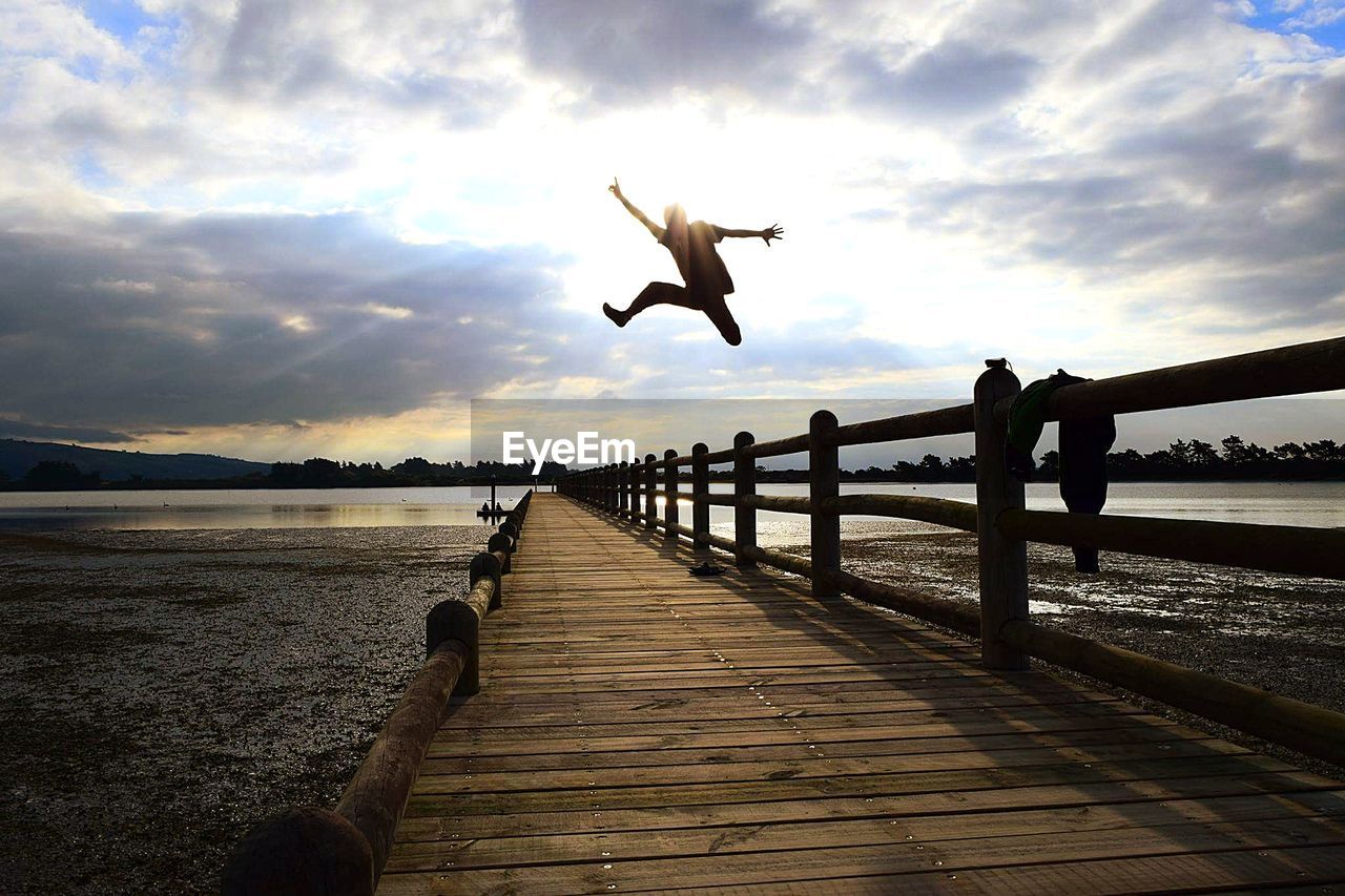 Low angle view of man jumping over pier against sky