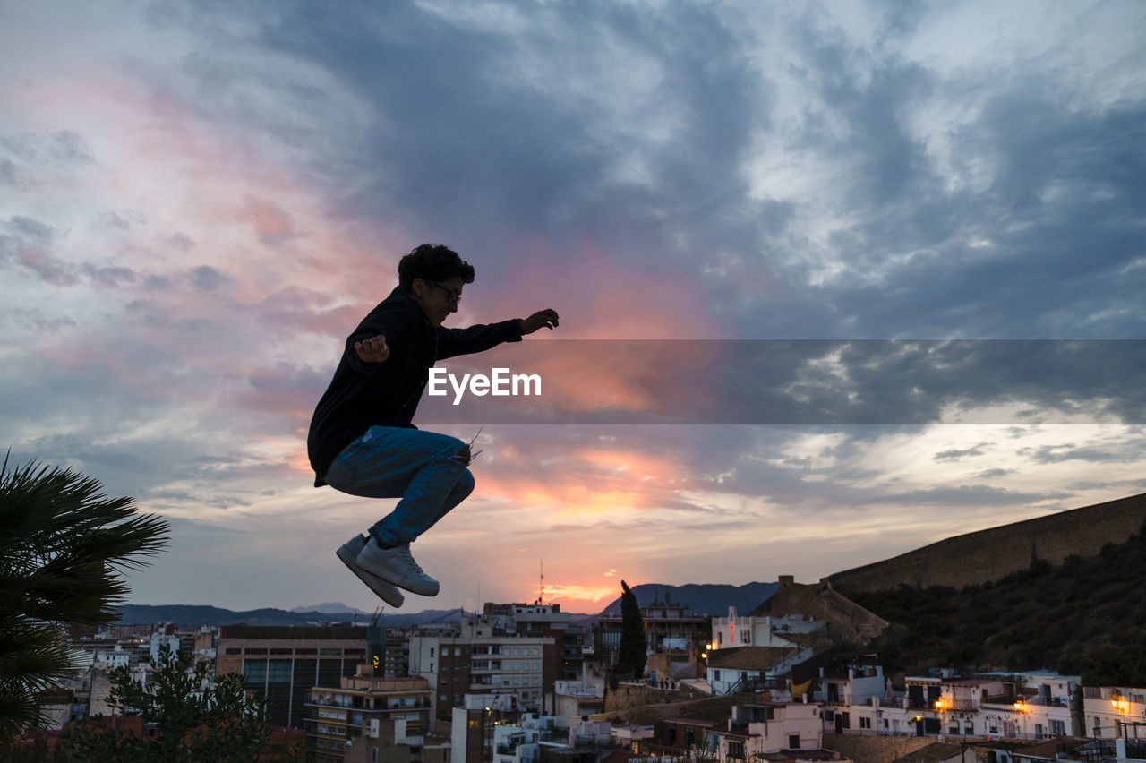 Silhouette of a person jumping outdoors with the sunset sky on background.