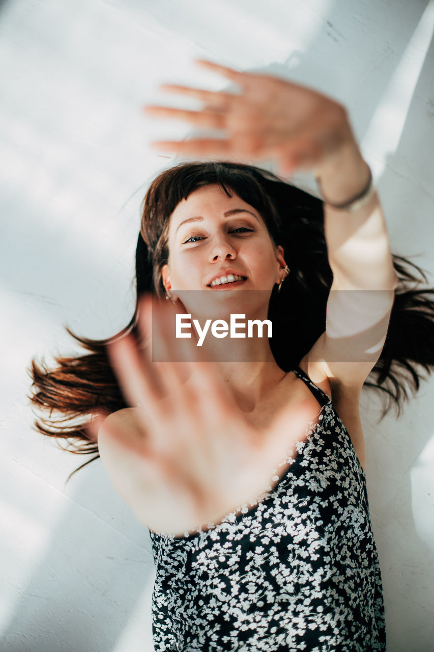 Portrait of smiling young woman gesturing against wall