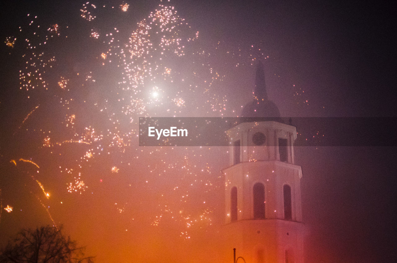 Low angle view of church and firework display against sky at night
