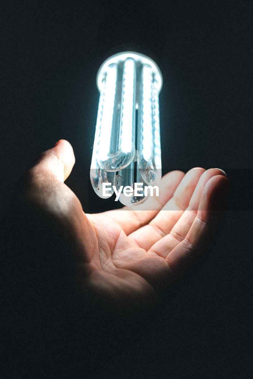 Led light bulb on illuminating a human hand on dark background