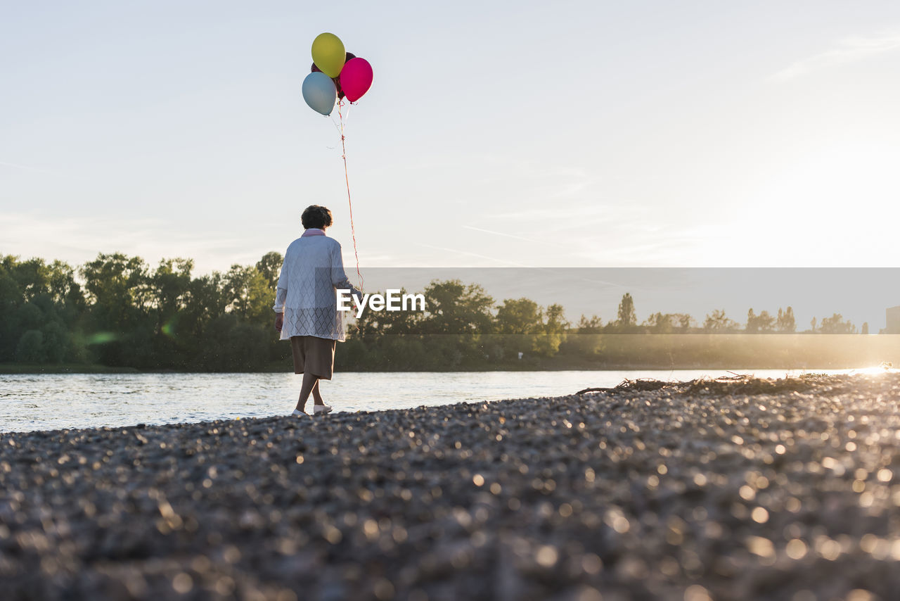 Back view of senior woman with balloons strolling at riverside