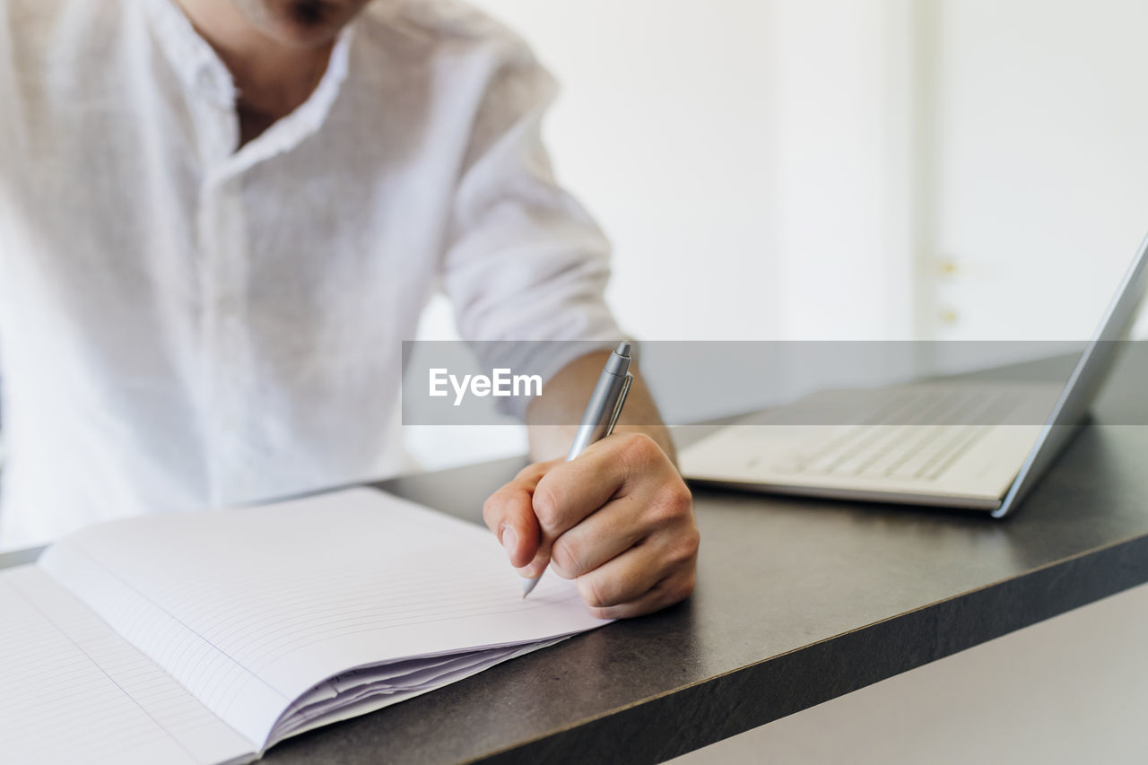 Man making list on book by laptop at kitchen island