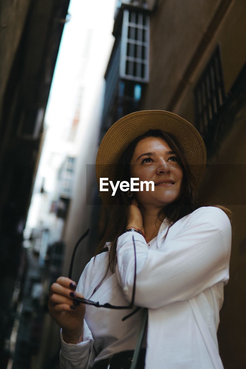 Low angle view of young woman wearing hat while standing against built structure