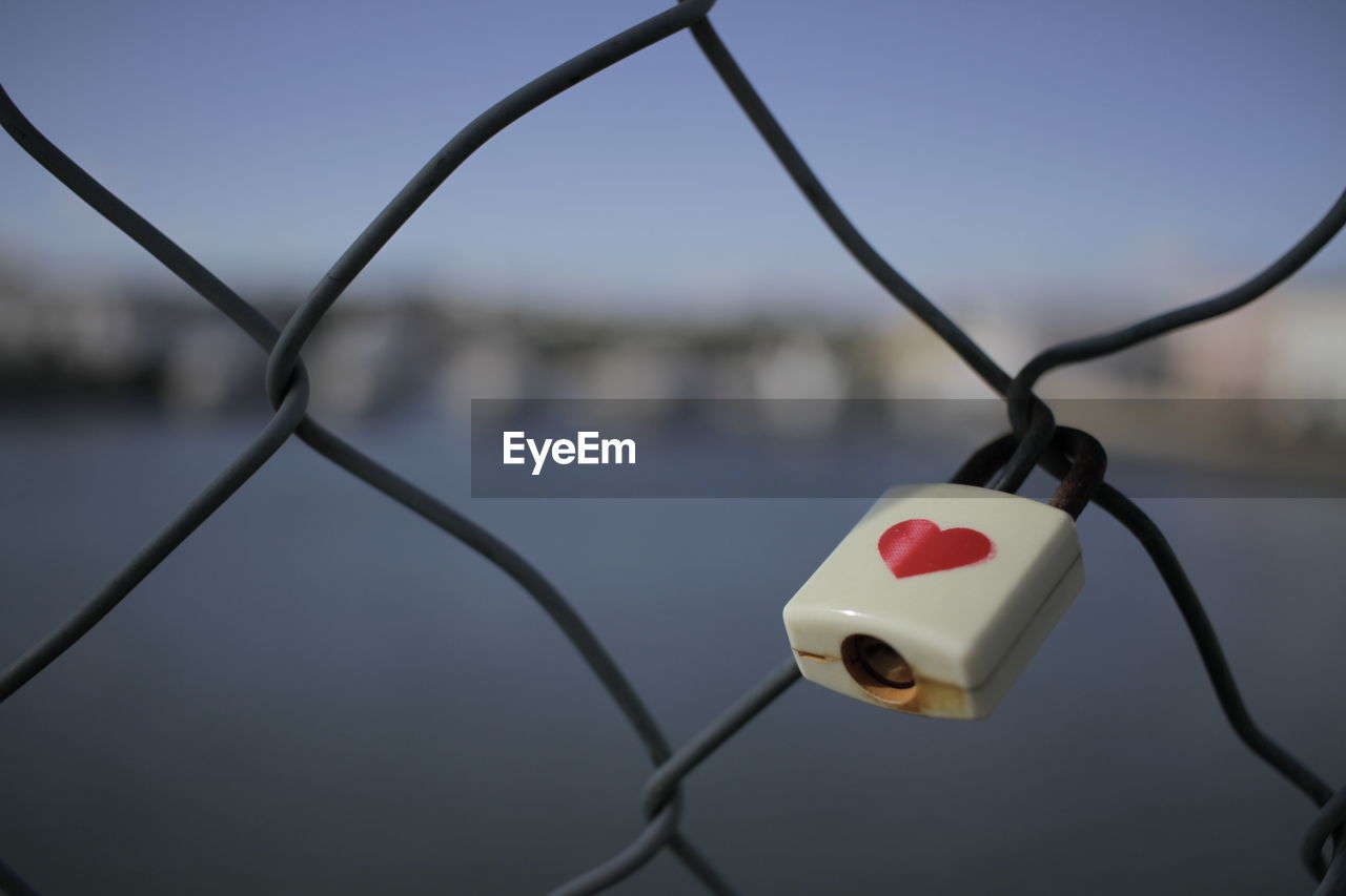 Close-up of padlock on chainlink fence against sea