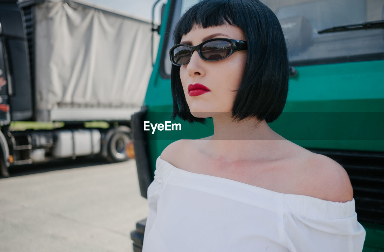 Young woman in sunglasses standing against truck