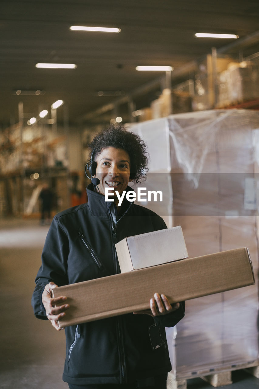 Smiling businesswoman with headset holding packages at warehouse