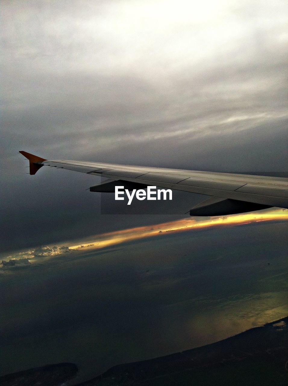 Airplane wing flying over sea at dusk
