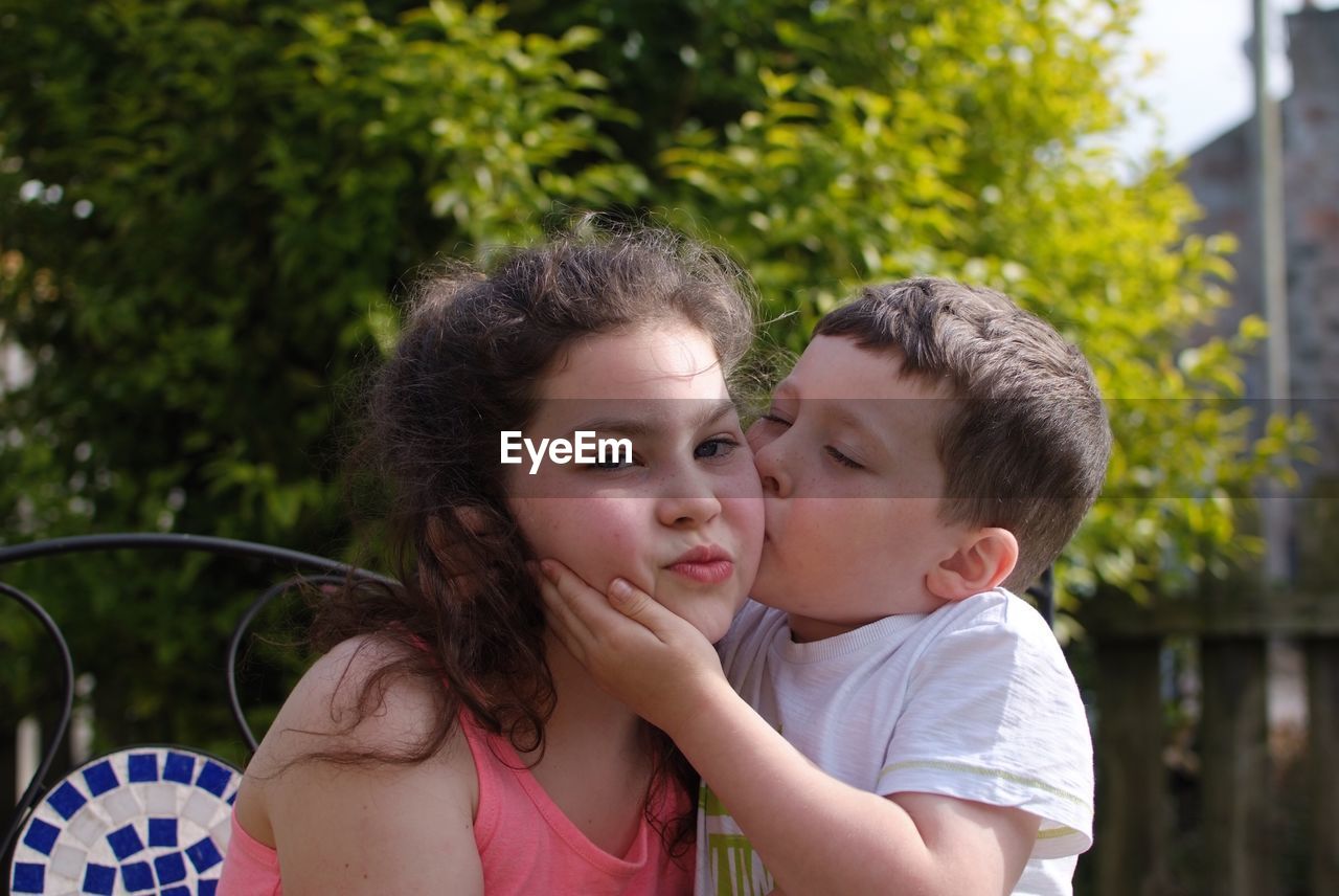 Brother kissing sister against trees