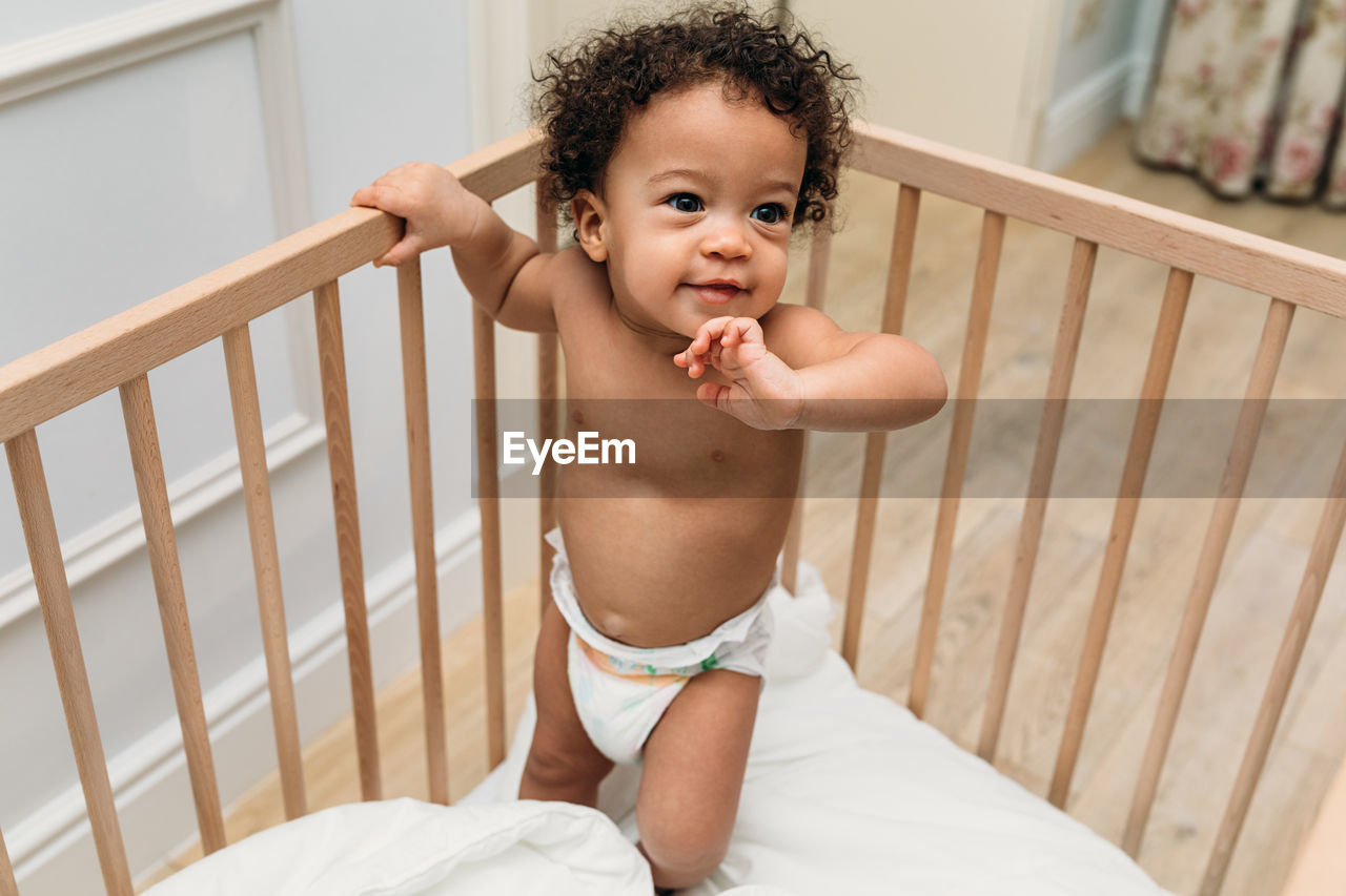 Smiling shirtless baby boy in crib at home