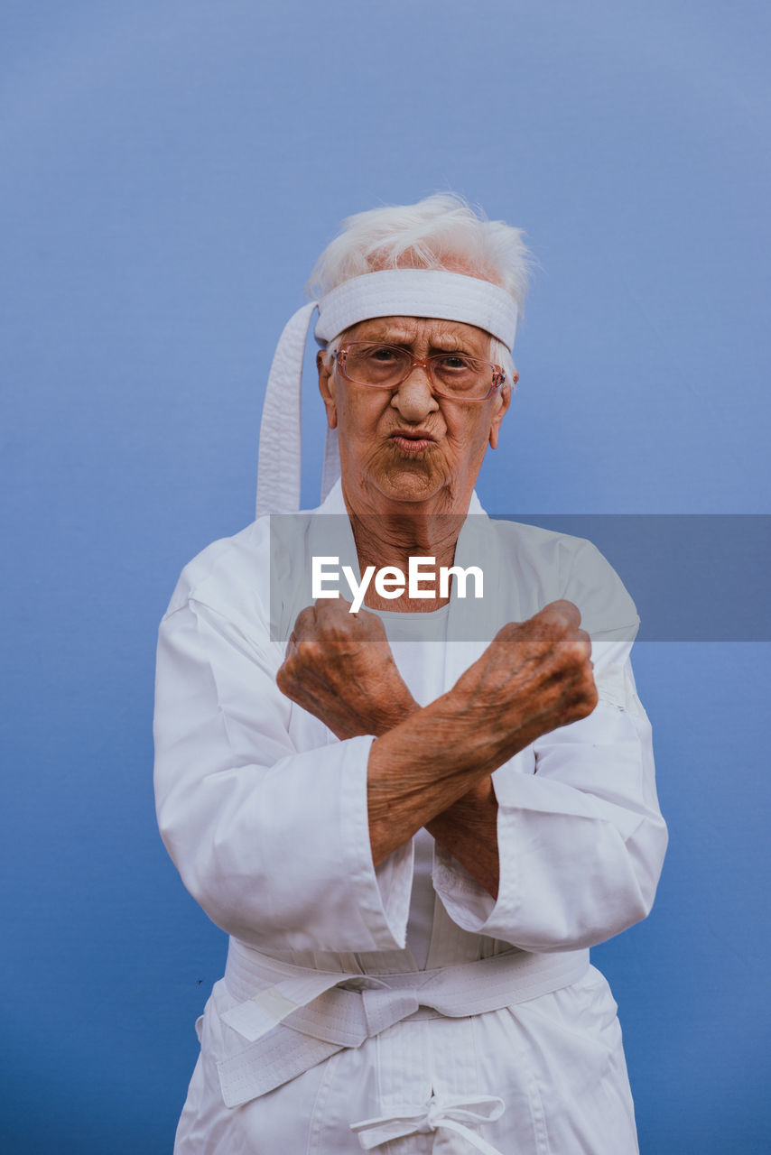 Portrait of senior woman doing karate against blue background