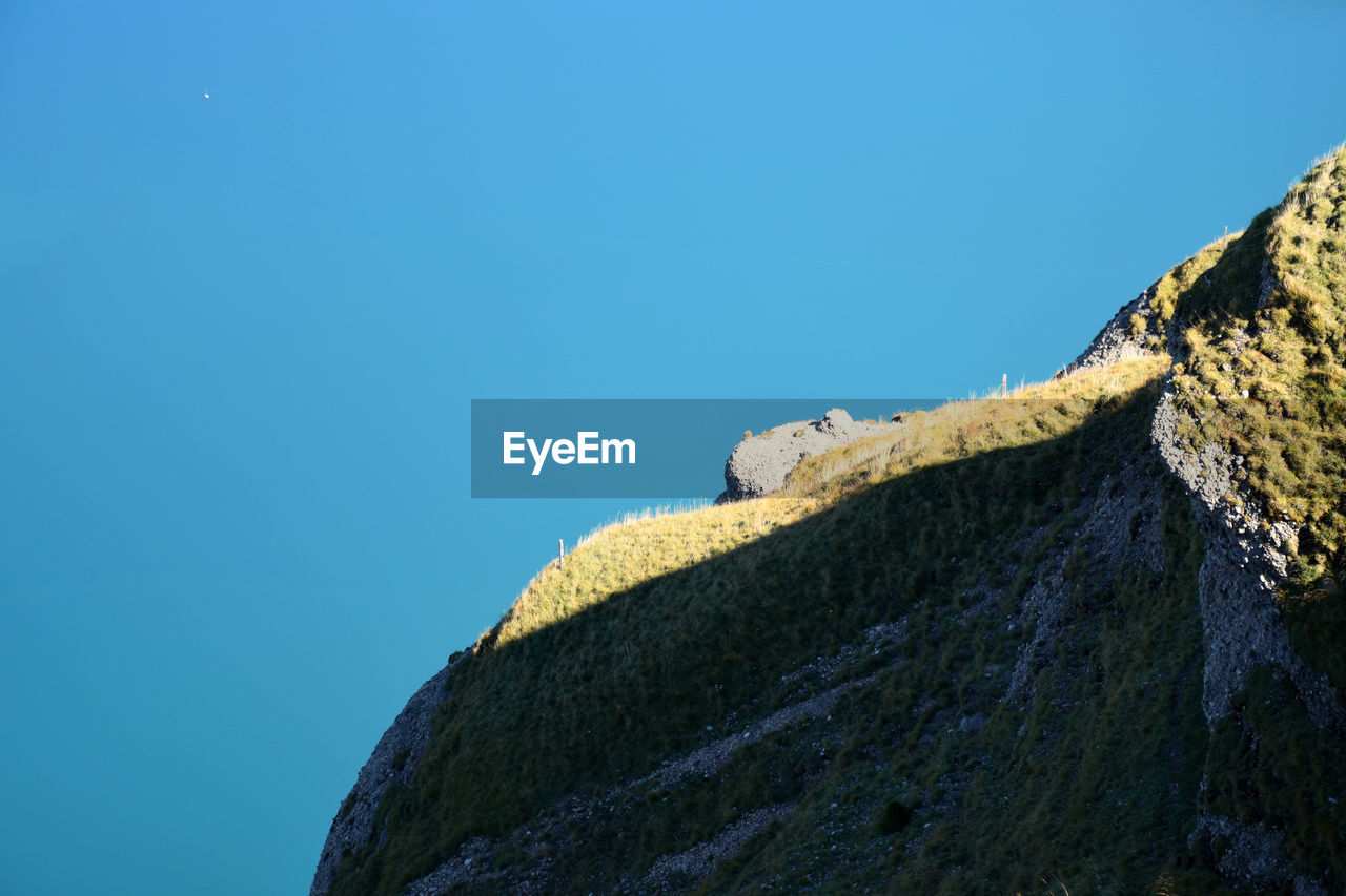 An oval shaped rock viewpoint on a hillside in the sun with lake zug in the background