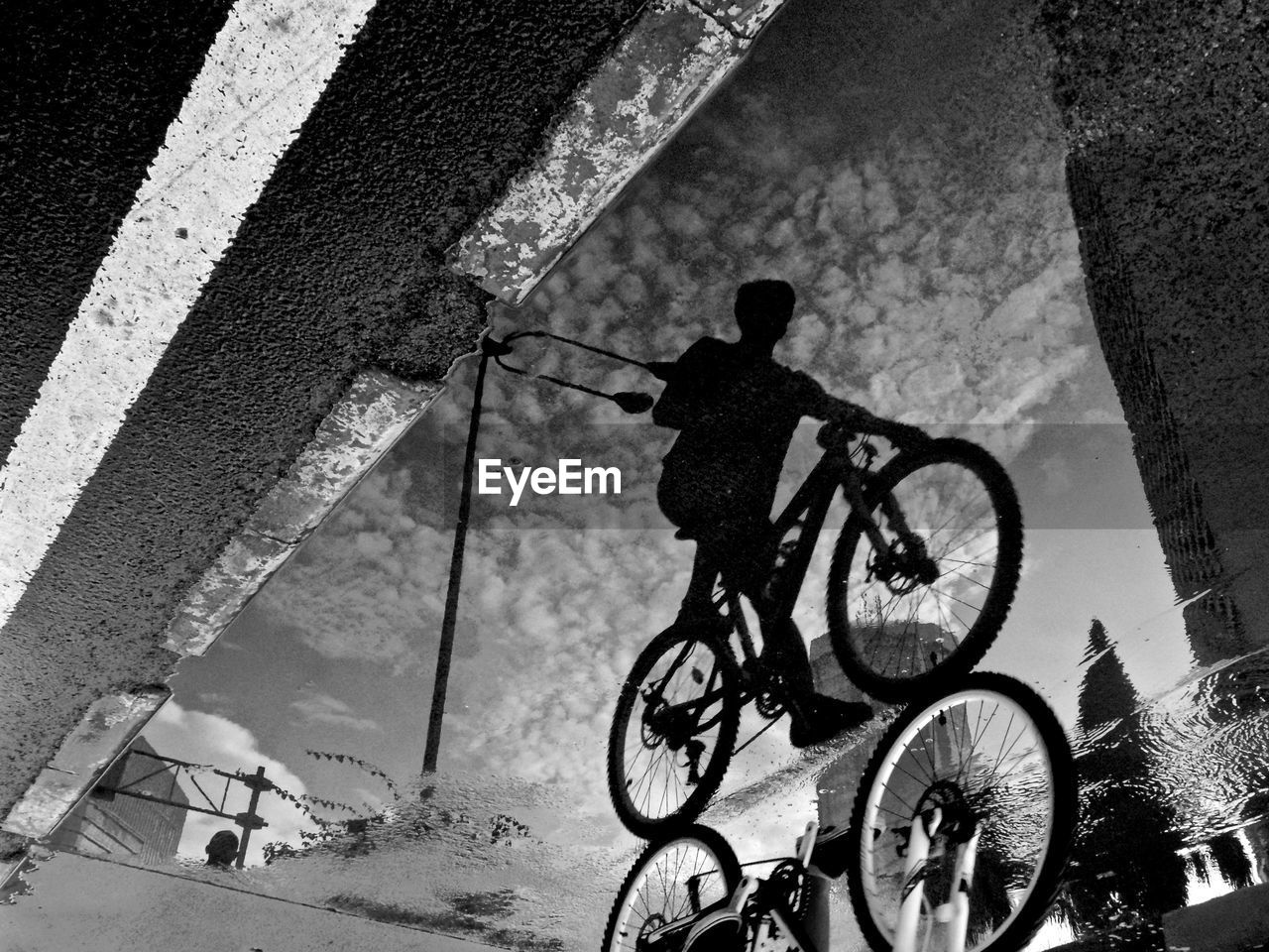 Reflection of man riding bicycle on puddle at street