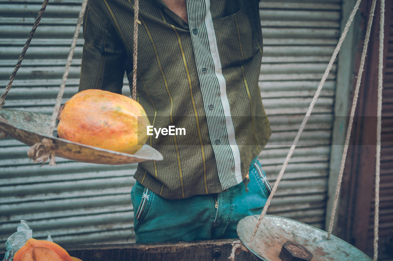 Midsection of man holding papaya on weight scale at market