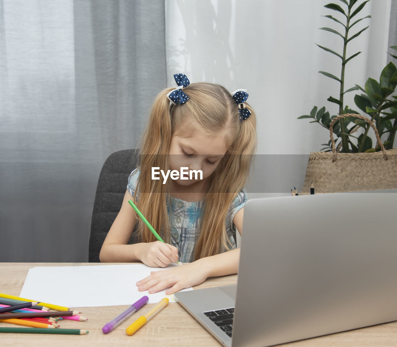 Girl drawing over paper by laptop on table