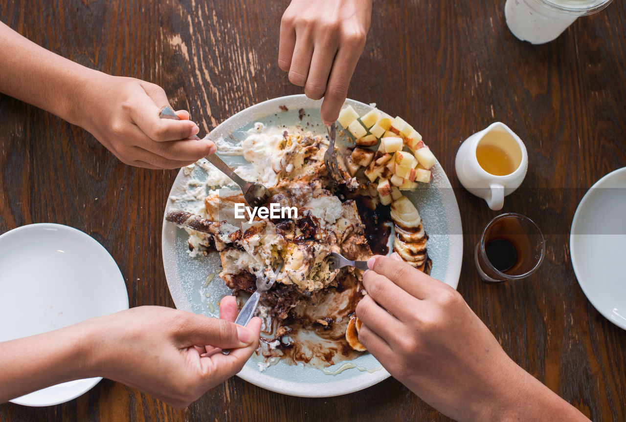 Cropped hands of people holding food in plate on table