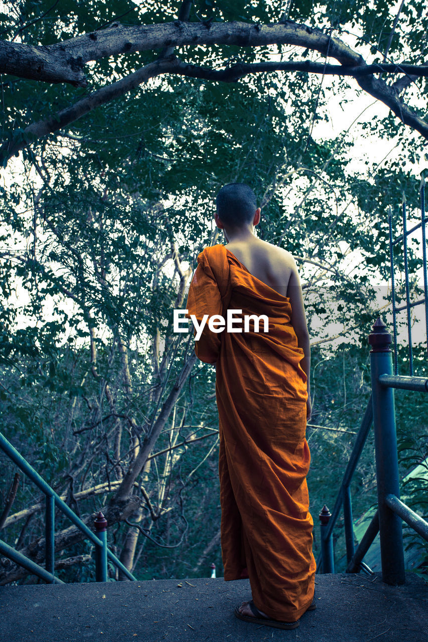 REAR VIEW OF MAN STANDING BY RAILING AGAINST TREE