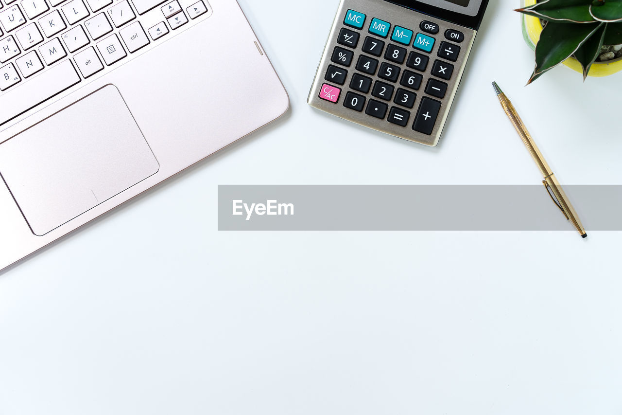 High angle view of laptop with calculator and pen on white background